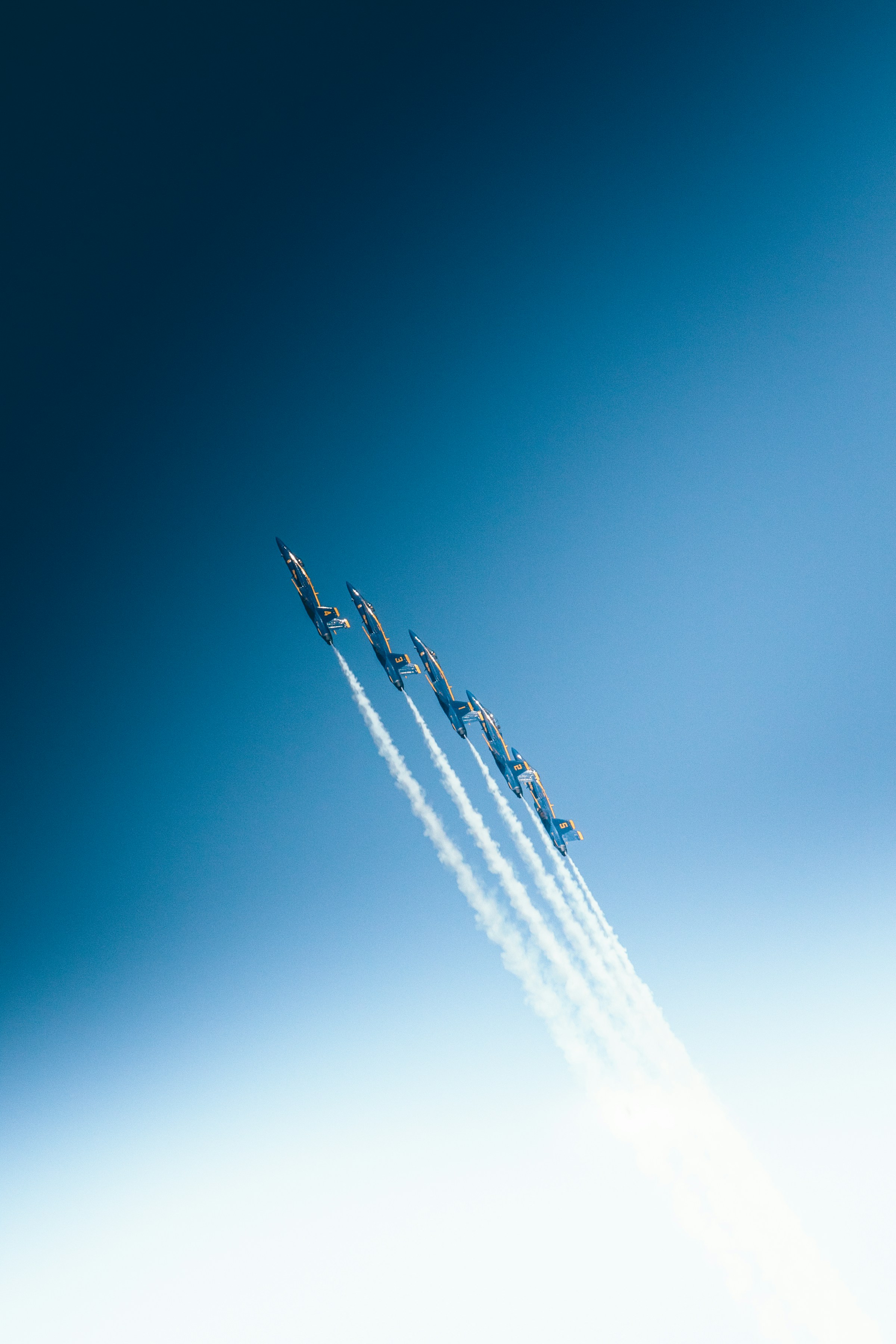 Five jet planes leaving a white trail in the blue sky.